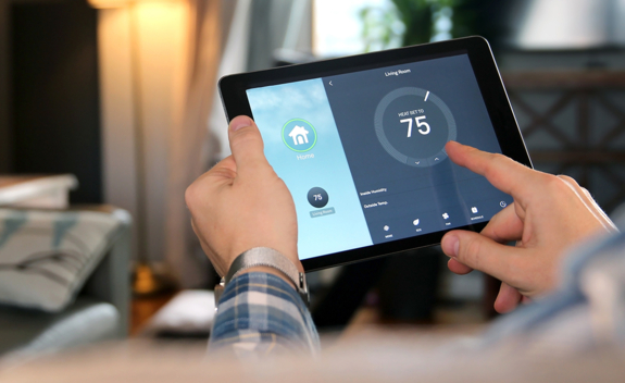 Hands holding a tablet device adjusting thermostat in their home digitally, with heat set to 75 degrees